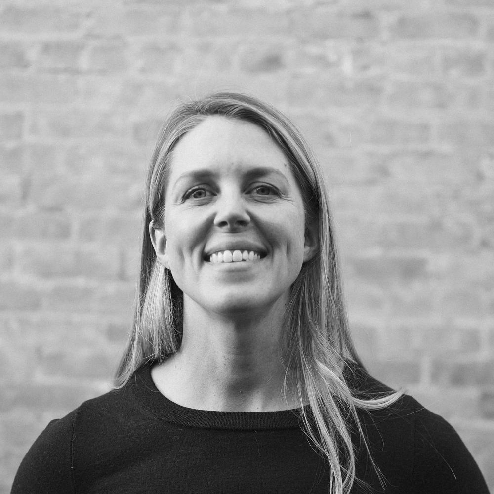 Smiling woman in black and white portrait with brick background.