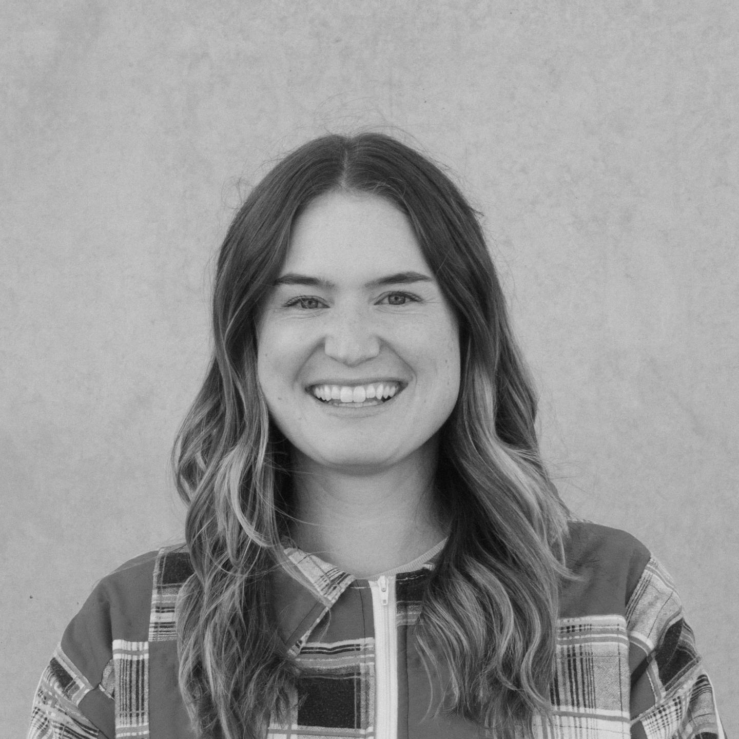 Smiling woman with long hair, wearing a plaid shirt. Black and white photo.
